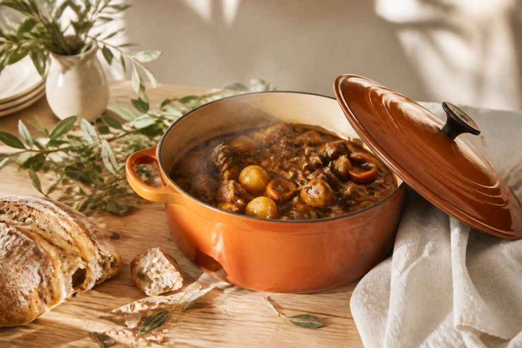 Cocotte en fonte émaillée terracotta sur une table avec mijoté fumant et pain frais
