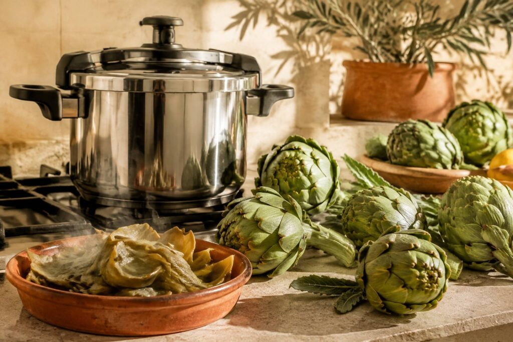 Cocotte minute avec artichauts verts frais sur un plan de travail en pierre ensoleillé